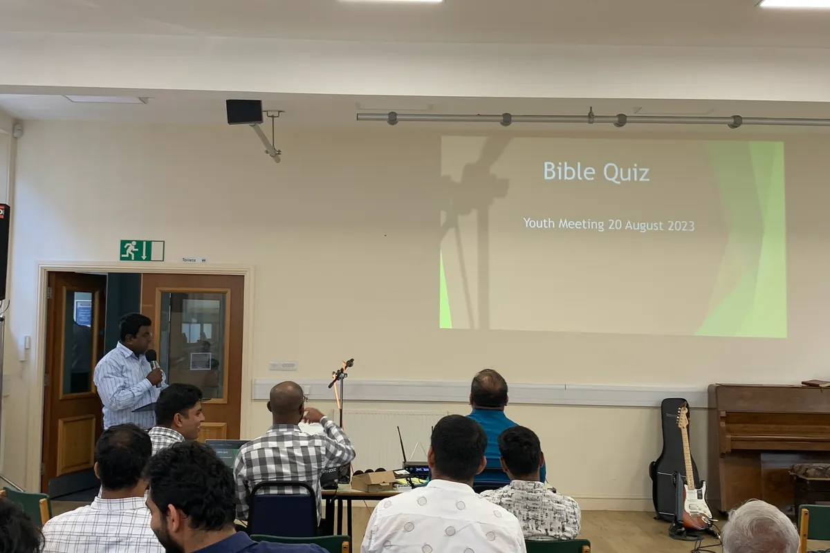 A youth leader hosting a Bible quiz, with the quiz on the screen behind